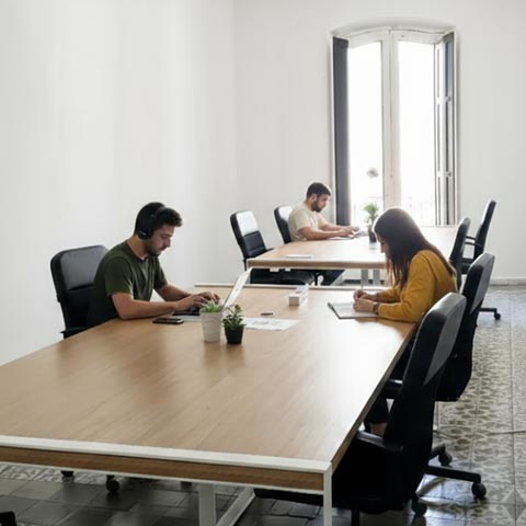 Personas trabajando concentradas en una mesa larga dentro de una sala de coworking silenciosa y luminosa.