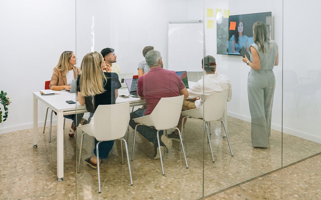 Equipo reunido en una sala de reuniones acristalada con presentación y videollamada