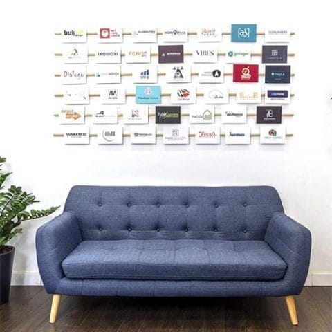 Sofá azul y muro con logotipos de empresas que usan la oficina virtual de Workspace Almería