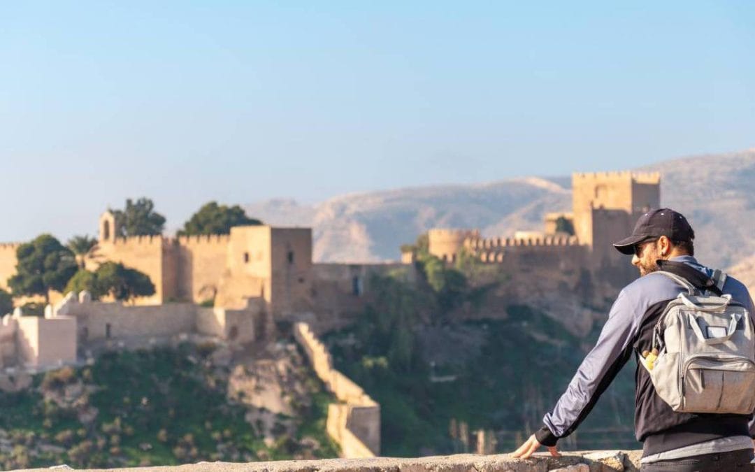Persona con mochila mirando la Alcazaba de Almería durante una estancia de teletrabajo en verano.